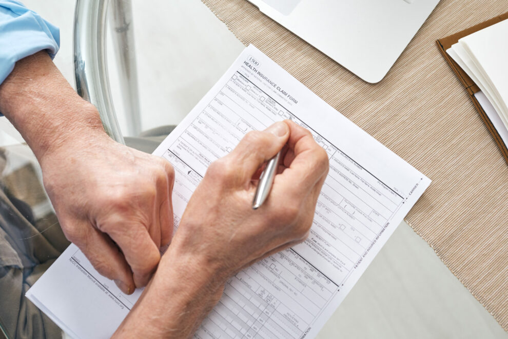 Hands of contemporary senior retired man filling in health insurance form